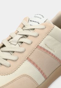 Sneaker de couleur claire avec un mélange de matériaux lisses et texturés, accents et lacets roses. Détail du logo doré sur le côté.