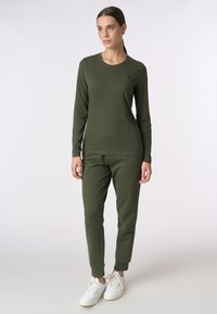 Camicia a maniche lunghe verde oliva e pantaloni abbinati realizzati in tessuto morbido, con scollatura rotonda e polsini affusolati, abbinati a sneaker bianche.
