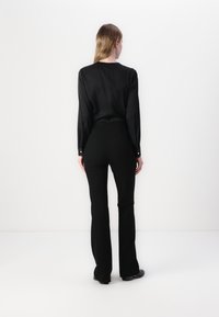 Svart langermet bluse med en glatt tekstur og løs passform, kombinert med høy midje svart flagrende bukser, med minimalistisk design.