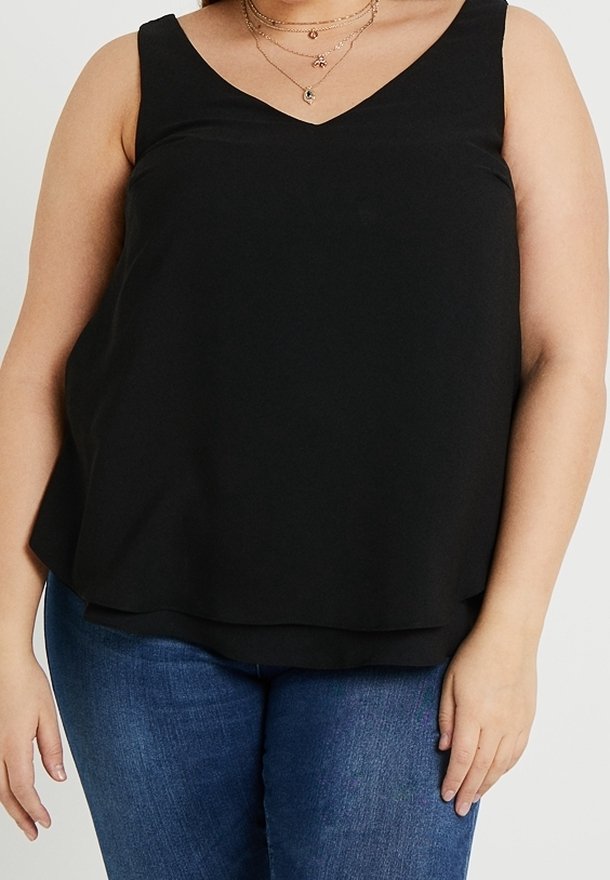 Top negro sin mangas con escote en forma de V, hecho de una tela suave, presenta un corte holgado y un dobladillo en capas. Se lleva con jeans de mezclilla azules.