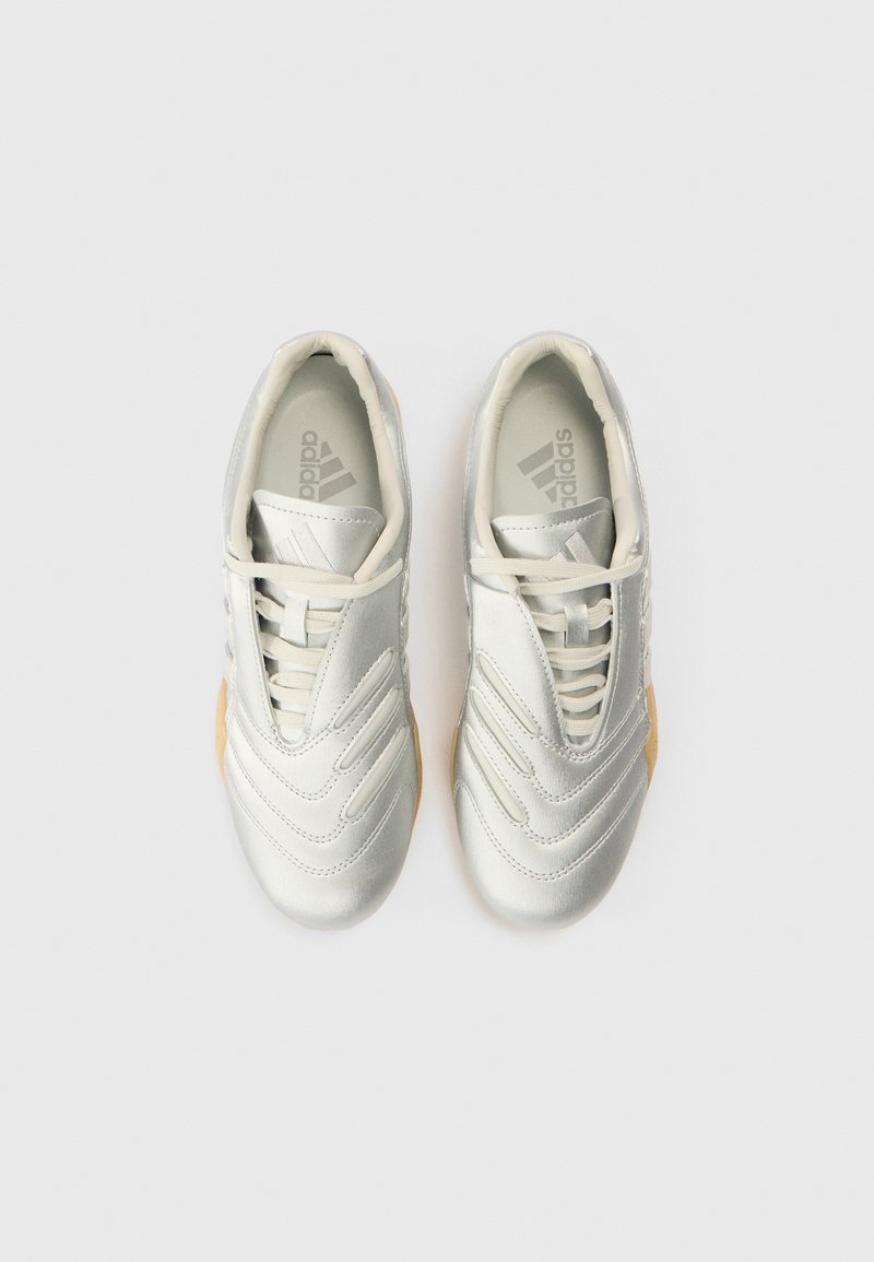 White athletic shoes with a smooth synthetic upper, featuring textured wave detailing, lace closure, and a gum rubber sole.