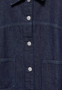 Veste en jean bleu foncé à l’avant avec boutons-pression argentés et deux poches rectangulaires visibles à l’avant de chaque côté.