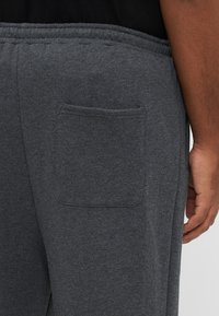 Γκρι φόρμα με πλαϊνή τσέπη στο πίσω μέρος και ελαστική μέση. Το ύφασμα έχει μαλακή υφή με μονόχρωμη επιφάνεια.