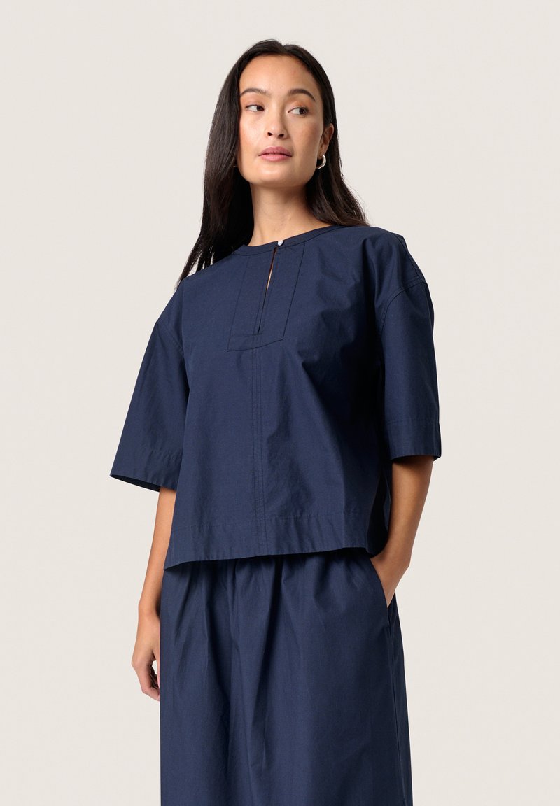 Navy blue short-sleeve top made of textured fabric, featuring a round neckline with a small front slit and straight cut.