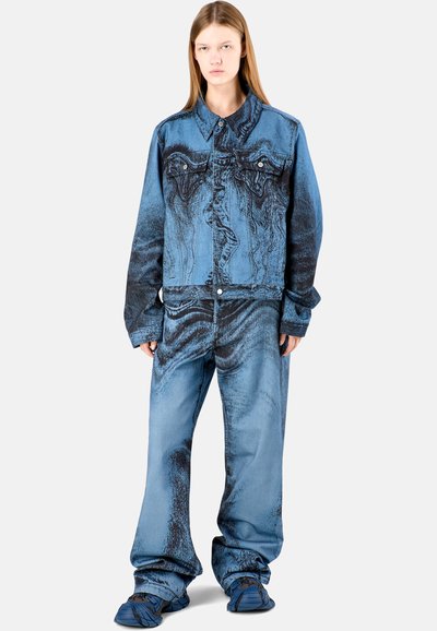 Completo in denim blu con motivi astratti scuri, composto da una giacca con bottoni sul davanti e pantaloni larghi.