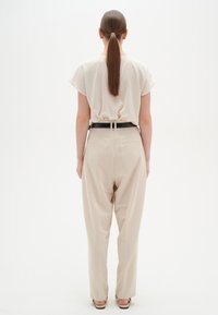 Beige afslappede bukser med sort bælte, parret med en matchende lys beige bluse, set fra ryggen. Glat stofstruktur.
