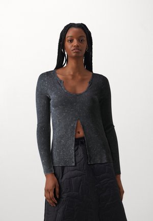 Black ribbed long-sleeve top with a round neckline and front slit detail. The fabric has a marbled texture, paired with a quilted black skirt.