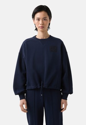 Sweatshirt bleu marine à manches longues, avec des poignets côtelés et un cordon de serrage à l'ourlet. Présente un patch texturé sur la poitrine gauche. Tissu lisse.