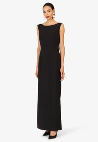 Robe longue noir sans manches avec encolure bateau, coupe ajustée, texture lisse et design longueur sol. Assortie à des chaussures à talons hauts noires.