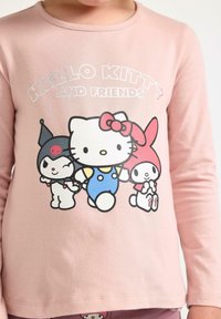 Maglietta a maniche lunghe rosa chiaro con una grafica di Hello Kitty e dei suoi amici vestiti in abiti colorati. Tessuto di cotone morbido con colletto a girocollo.