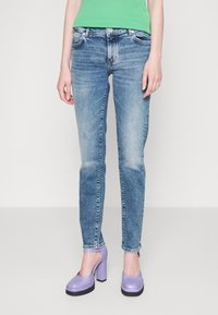 Jeans de mezclilla de color azul claro con un diseño ajustado, zonas descoloridas, cinco bolsillos y un acabado ligeramente desgastado, combinados con zapatos de plataforma morados.
