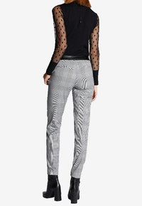 Haut noir avec des manches en tulle à pois, associé à un pantalon à carreaux gris et des bottes à talons épais noires. Matériaux texturés visibles.