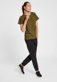 Olivengrøn kortærmet t-shirt med afslappet pasform, kombineret med sorte joggerbukser og sorte sneakers. Enkel design og glat tekstur.