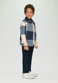 Blauw en crèmekleurig geruit flanellen overhemd, met knopen en gedragen over een wit T-shirt, gecombineerd met donkere cargobroeken en witte sneakers.