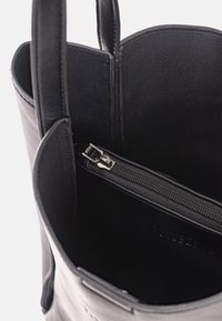 Interno di una borsa a spalla nera in pelle con una tasca con zip. Texture liscia, design strutturato e due manici robusti.