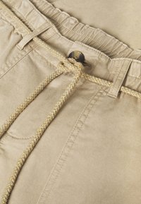 Bermudas de algodón beige con cierre de cordón, que cuentan con un cordón texturizado dorado y un botón. Tejido suave con detalles de costura sutiles.