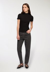 Czarny dopasowany top z krótkim rękawem zestawiony z ciemnoszarymi spodniami z wysokim stanem i płaskimi czarnymi butami z ćwiekami.