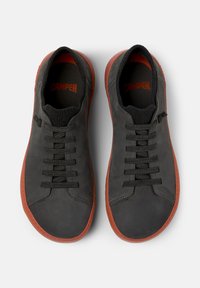 Black leather sneakers with a textured finish, round toe, black laces, elastic collar, and red rubber sole. Brand "Camper" embossed inside.