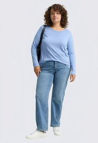 Világoskék hosszú ujjú felső, egyenes szárú kék farmerrel, fehér sportcipővel viselve, fekete válltáskával.