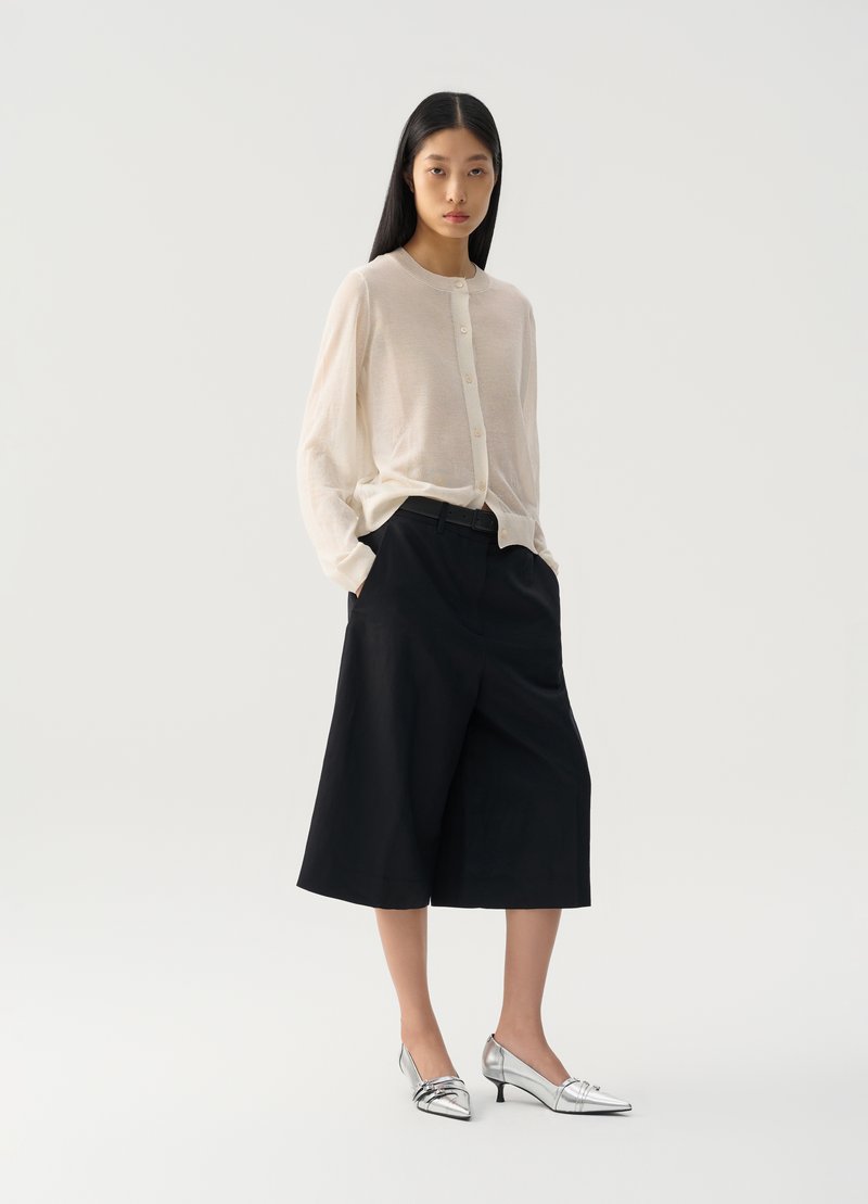 Camicia button-up beige chiaro, pantaloni corti a gamba larga blu navy e scarpe con tacco a punta argento. Tessuto liscio, vestibilità rilassata e design minimalista.