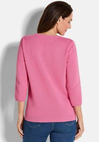 Rosa Strickpullover mit drei Viertelärmeln, strukturiertem Muster, geripptem Ausschnitt und Saum, kombiniert mit blauen Jeans.