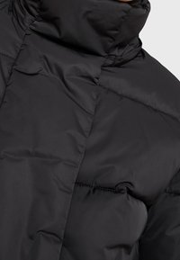 Giacca a vento nera con colletto alto, texture liscia e pannelli cuciti per l'isolamento. Il tessuto sembra leggero ma caldo.