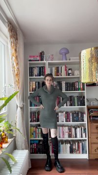 Abito maglione verde oversize, con collo a scialle, abbinato a stivali neri alti fino alla coscia. Presenta una texture a coste e una silhouette aderente.