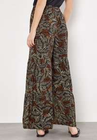Flowy, wide-leg pants in black fabric with a colorful fern leaf print in gold and rust. Features a high waist and soft texture.