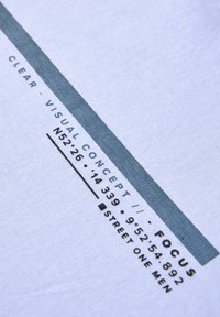 Tissu blanc présentant un texte imprimé en noir et bleu. Le design inclut des coordonnées géographiques et la marque 'STREET ONE MEN'.