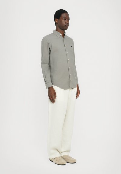 Siva srajca s dolgimi rokavi, kombinirana z belimi širokimi hlačami in bež natikači. Preprost, minimalističen dizajn.