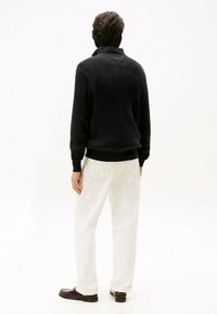 Schwarzer gerippter Pullover mit hohem Kragen, kombiniert mit beigen, lässigen Hosen und dunkelbraunen Schuhen. Schlichtes und strukturiertes Design.