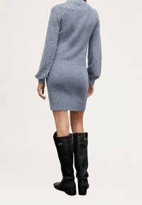 Grå stickad klänning med lång ärm, prydd med pärl-accenter på axlarna, tillsammans med knähöga svarta läderstövlar.