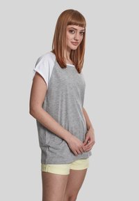 Grå kortærmet t-shirt med hvide raglanærmer, afslappet pasform, parret med lysegule shorts. Glat tekstur og afslappet design.