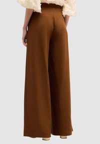 Pantaloni a gamba larga in un ricco tessuto marrone, con una vita alta e una superficie liscia, caratterizzati da un design minimalista e senza motivi visibili.