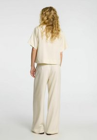 Beige cropped top med korte ærmer parret med brede bukser lavet af glat stof med en subtil glans. Ingen mønstre eller accenter synlige.