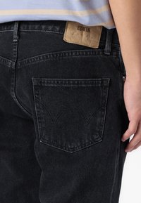 Jean en denim noir avec un tissu texturé, présentant une poche arrière avec un design cousu et une étiquette en cuir tan marquée "EDWIN."