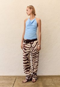 Top a halter azzurro chiaro con scollo drappeggiato, abbinato a pantaloni larghi a righe zebrate beige e marroni. Cintura marrone e sandali marroni.