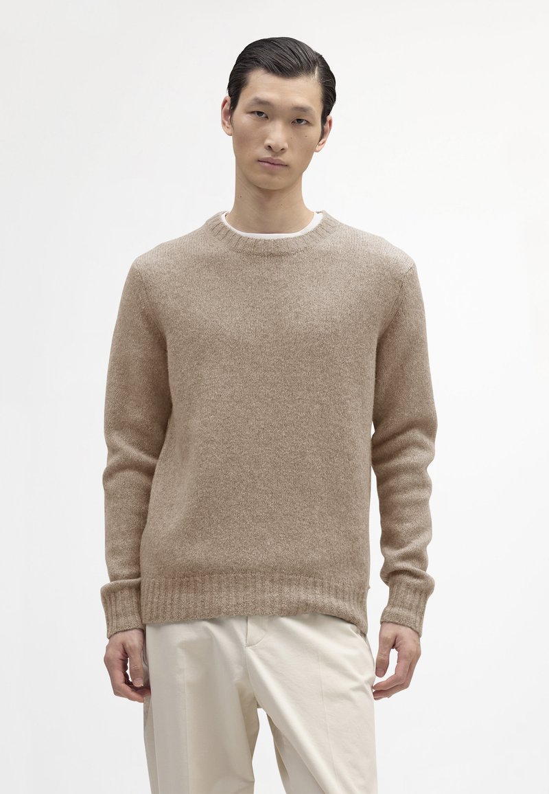 Beige gebreide trui met een ronde halslijn en ribgebreide manchetten, gemaakt van zacht, gehaakt stof. Gecombineerd met lichte broeken.