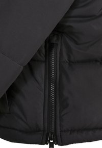 Blouson matelassé noir en gros plan montrant une fermeture éclair noire verticale avec du tissu entourant les dents de la fermeture.