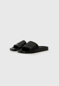 Sandales noires en caoutchouc avec un logo en relief sur les brides. Design open-toe avec une semelle plate et une texture lisse.