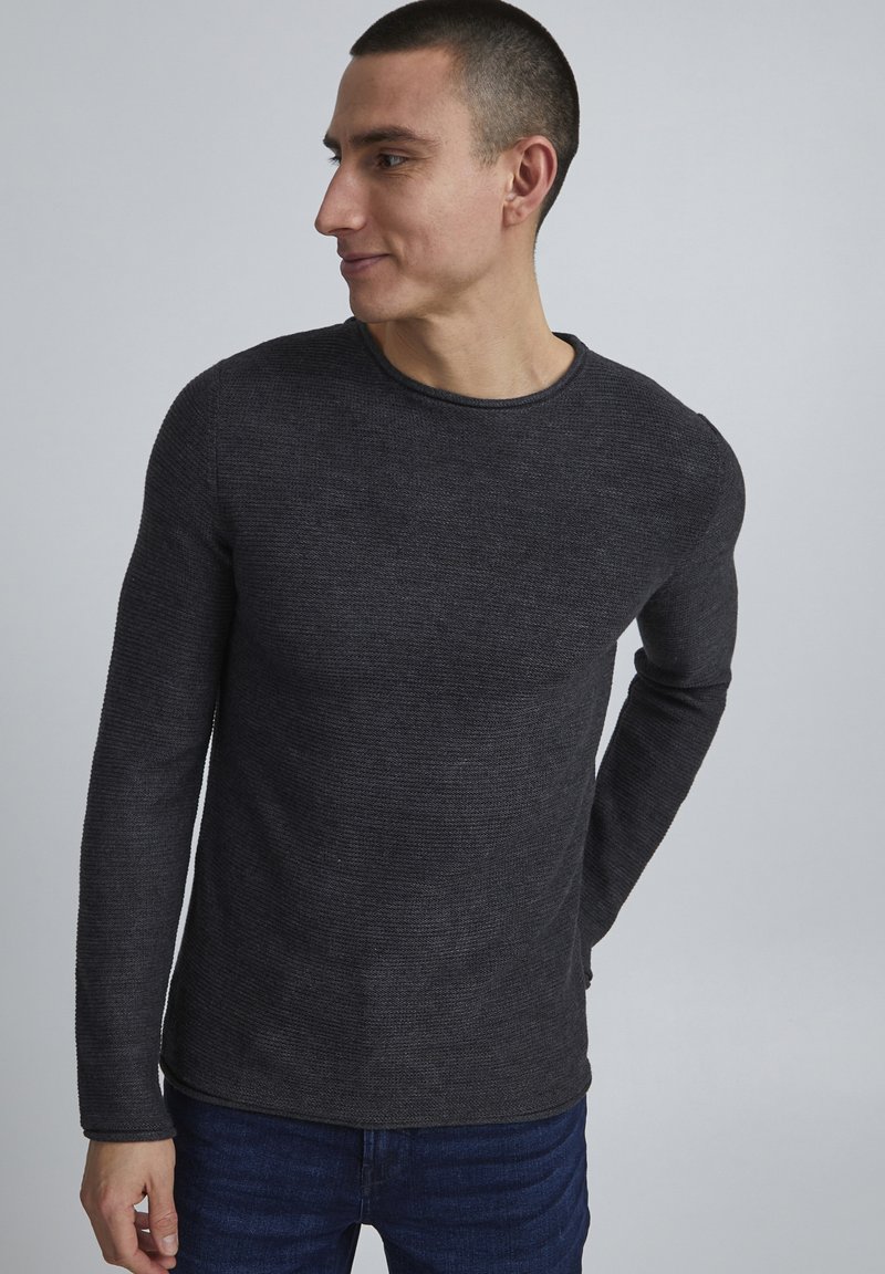 Suéter de punto gris de manga larga con cuello redondo, patrón texturizado y un diseño ajustado. Combinado con pantalones de mezclilla.