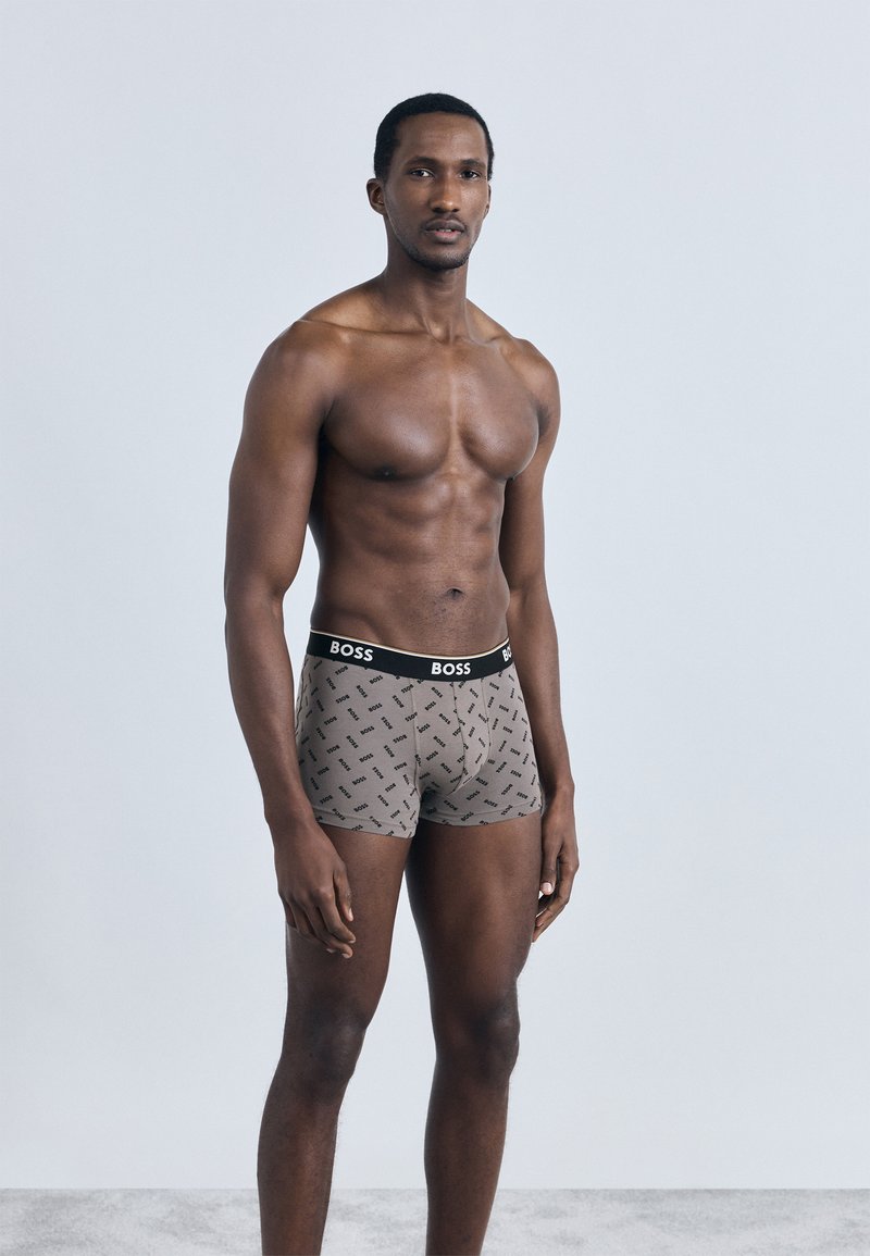 Hnědé boxerky z měkké látky, s černým pasem s logem "BOSS" a jemným vzorem po celé ploše. Pružný střih.
