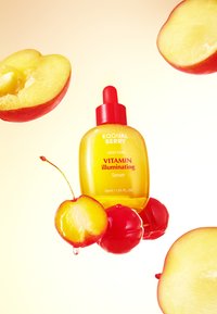 Żółta butelka serum z czerwoną zakrętką pipety, otoczona połówkami czerwonych jabłek, ukazująca błyszczącą teksturę i żywe kolory. Widoczne etykiety.