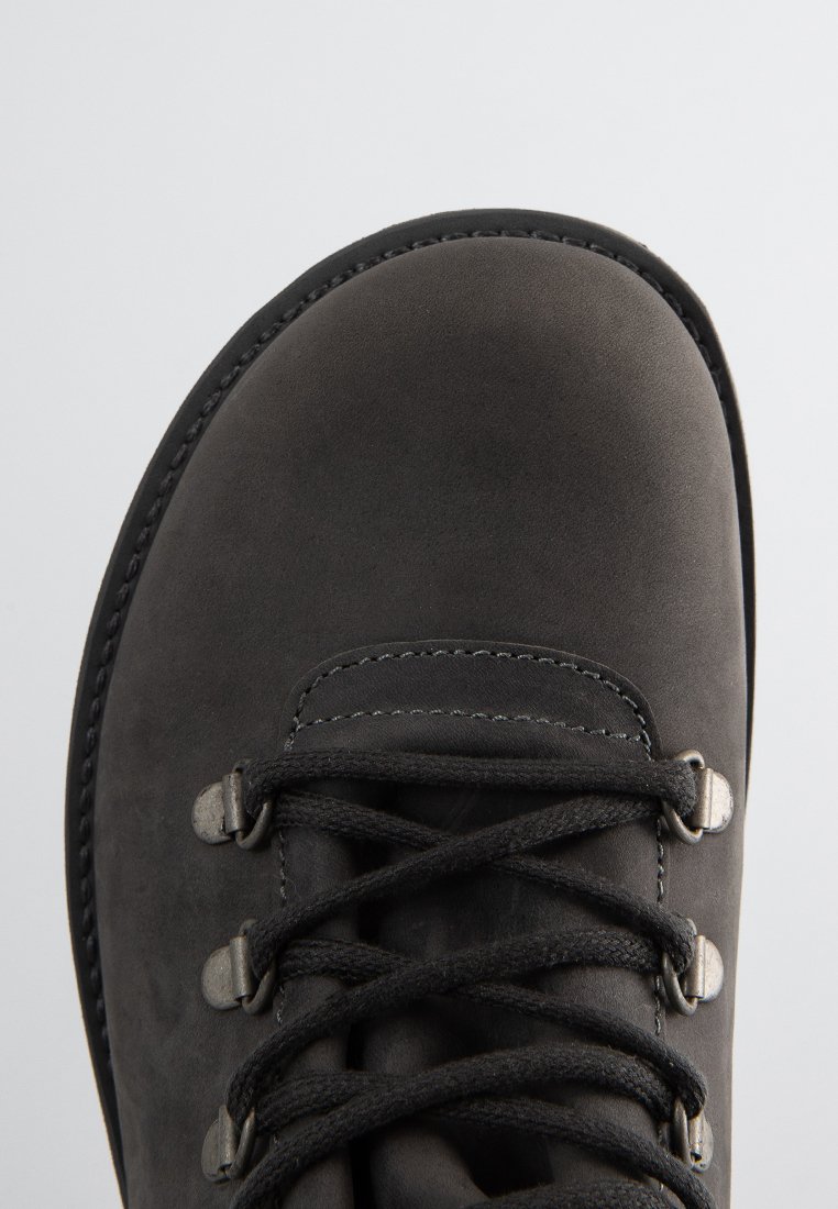 Nahaufnahme der Zehe eines schwarzen Lederwanderschuhs mit metallenen Ösen und schwarzen Schnürsenkeln, die im Kreuzmuster gebunden sind.