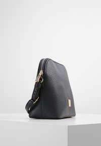 Marineblå tekstureret lædertaske med guldlynlås og metaldele, der har en rektangulær form og en justerbar skulderrem.