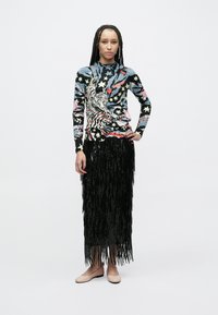 Top de manga larga multicolor con patrones de tigres y estrellas; falda negra con flecos y lentejuelas; zapatos planos de color claro. Diseño sencillo y moderno.