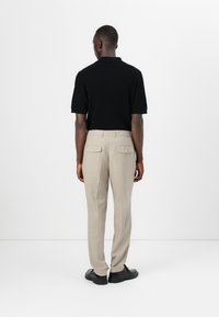Polo noir à manches courtes côtelé associé à un pantalon beige clair ajusté et des chaussures noires, vu de dos.