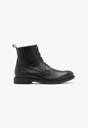 Botín de cuero negro con un acabado liso, punta redonda, diseño con cordones y un sutil detalle de costura en la parte superior y lateral.