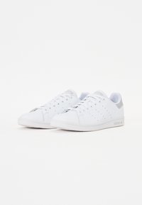 Hvide lædersneakers med en glat overflade, der har perforeringer på siderne, grå detaljer på hælen og en struktureret hvid sål.