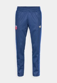 Calças de treino azul-marinho feitas de tecido suave, com uma cintura elástica, riscas laterais azuis e um logo dourado da Adidas no quadril esquerdo.